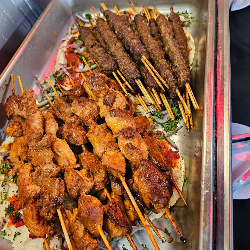 A catering tray filled with rows of grilled chicken and beef kebabs on skewers.