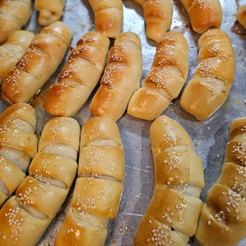 Close-up of golden-brown baked pastries, possibly cheese rolls or breadsticks, sprinkled with sesame seeds.