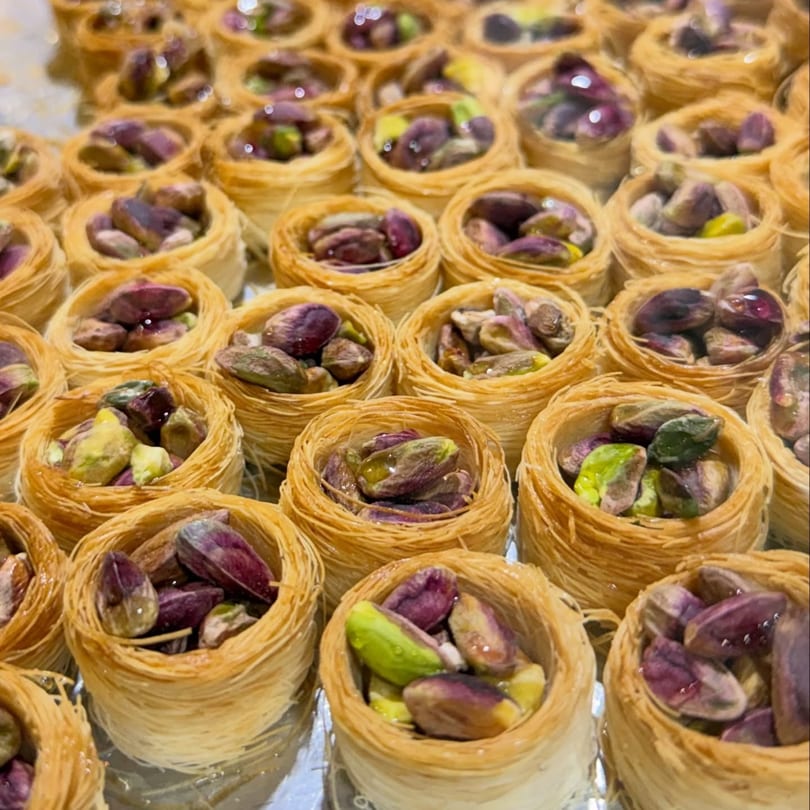 Close-up of numerous bird's nest baklava pastries, each filled with vibrant green and purple pistachios.